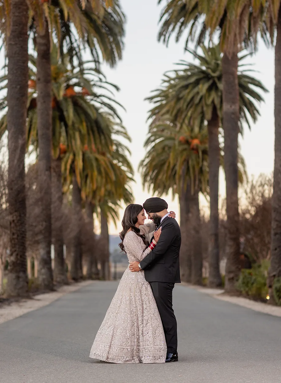 Couple embracing on a tree-lined path between towering palm trees at golden hour