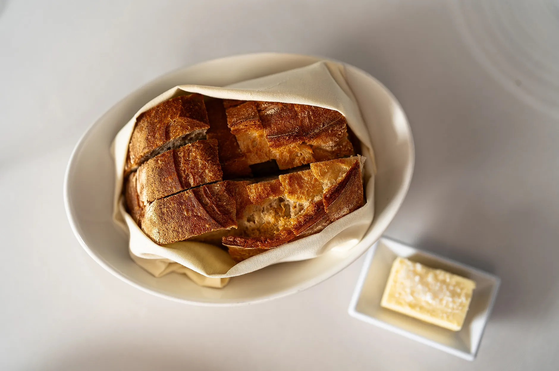 Sliced artisan bread wrapped in cloth inside an oval dish with a side of butter