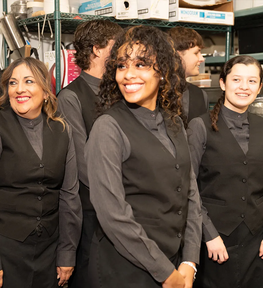 Catering staff in black uniforms laughing together in the kitchen before an event