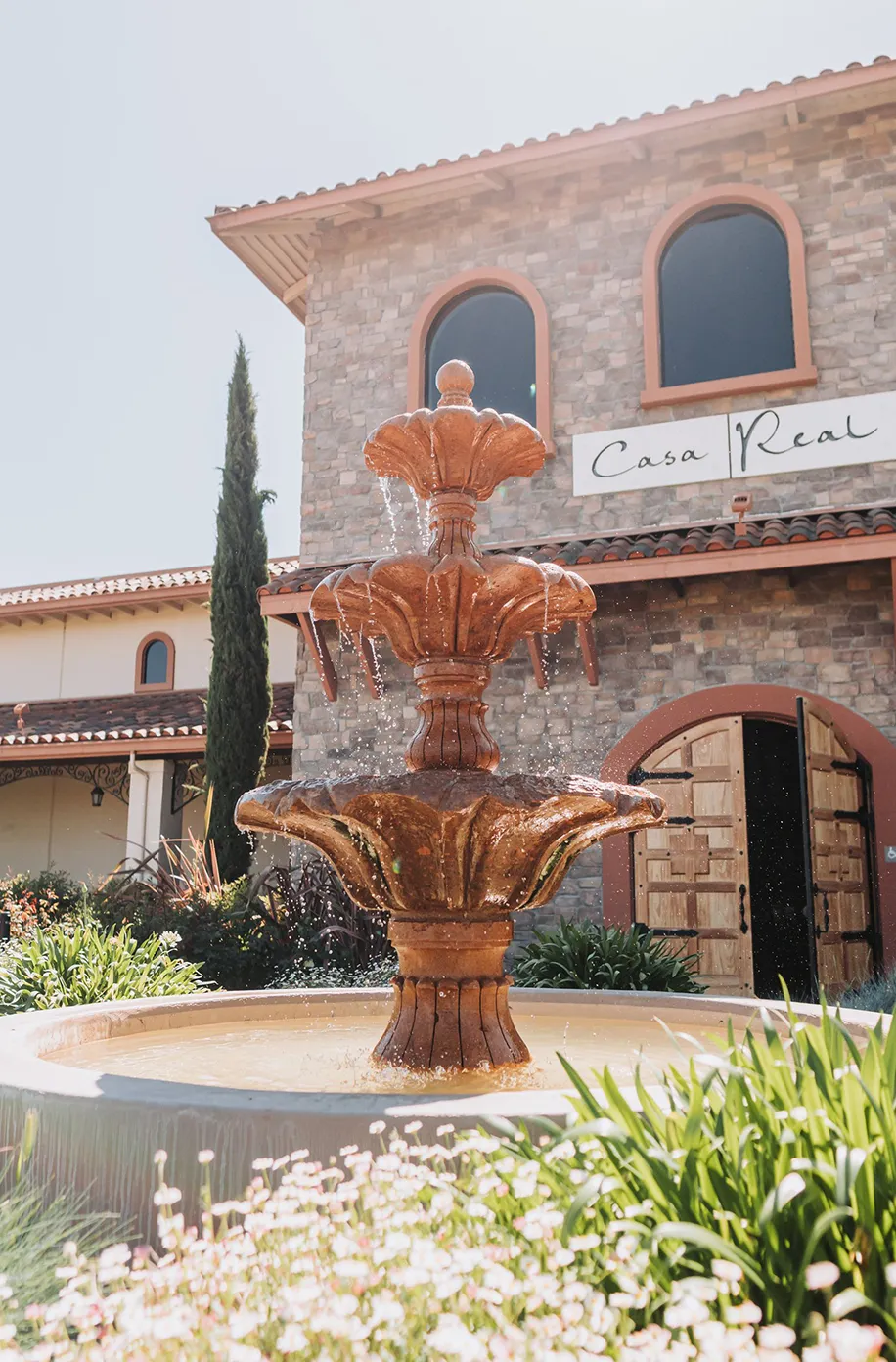 Tiered copper fountain in the Casa Real courtyard with the stone building and cypress tree in the background