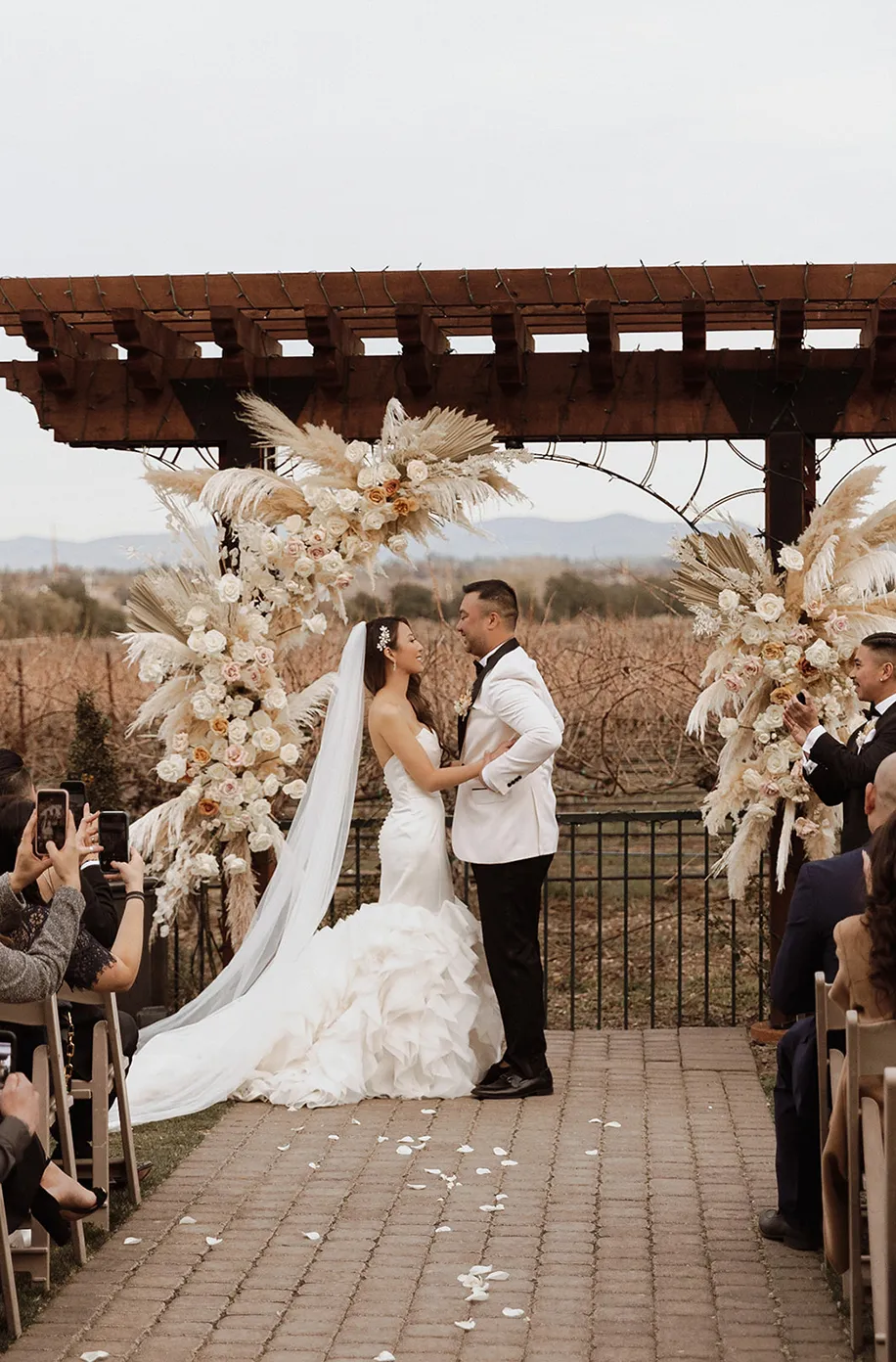 Bride and groom sharing a kiss under a pergola with dried floral and pampas grass arrangements