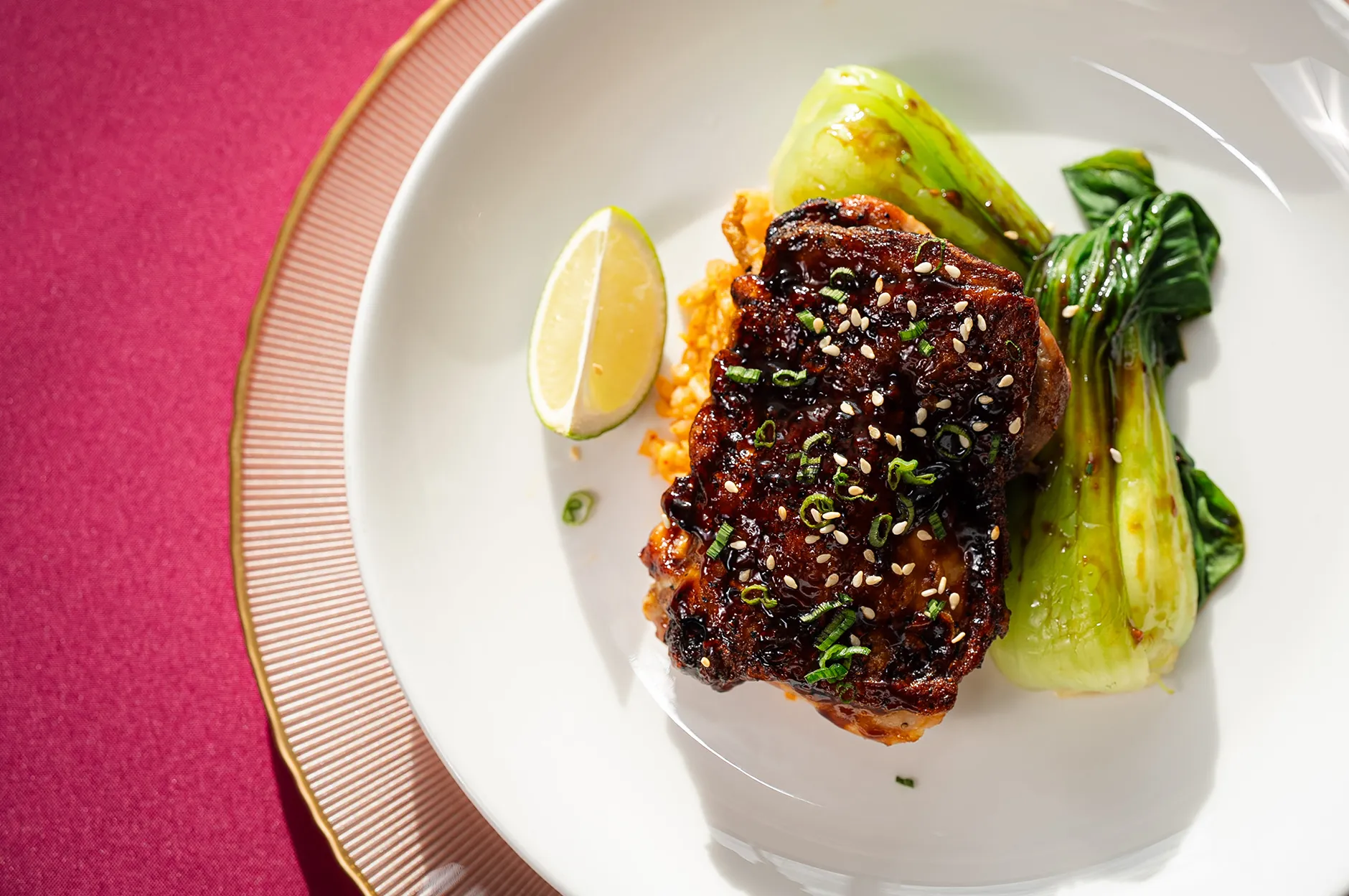 Sesame-glazed short rib with sautéed bok choy and a lime wedge on a gold-rimmed plate