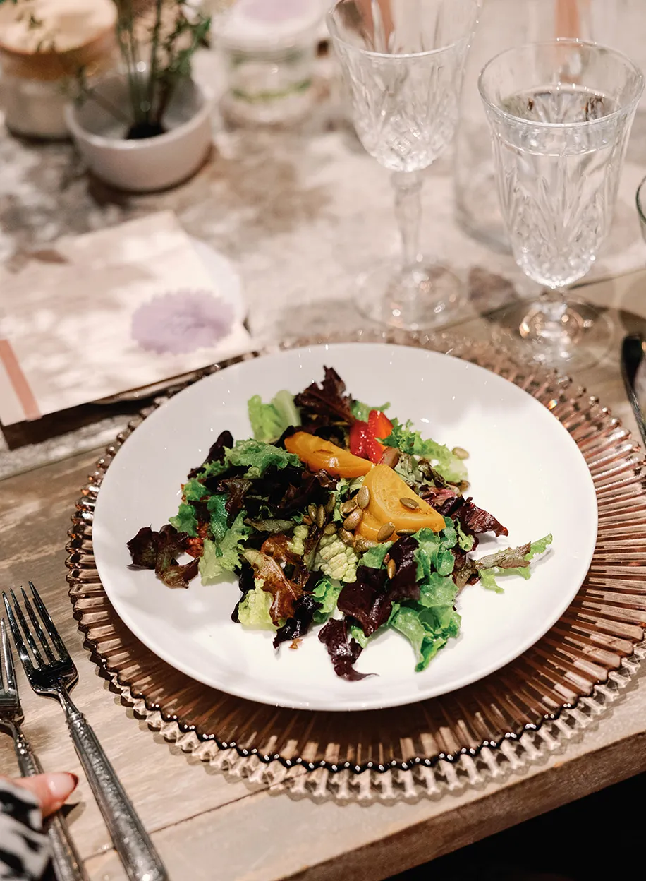 Mixed green salad with roasted vegetables on a beaded gold charger plate at a formal table setting
