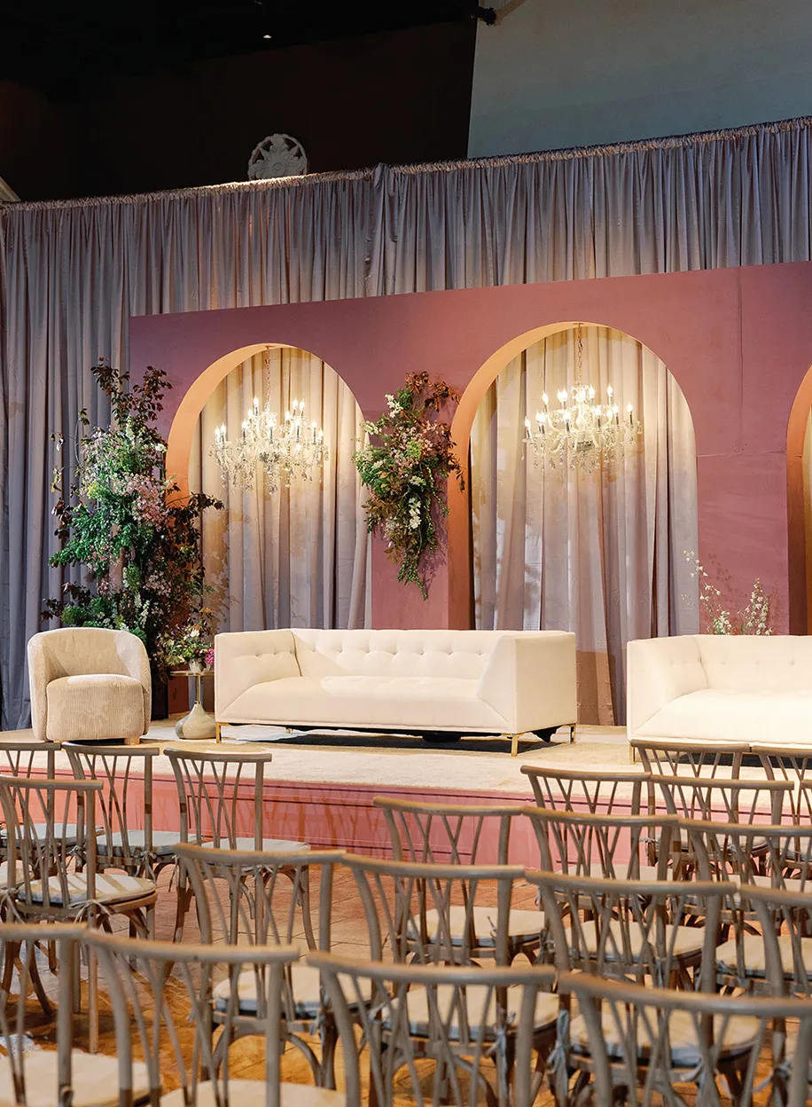 Stylish lounge area with tufted white sofas, arched mauve backdrop panels, crystal chandeliers, and rattan seating