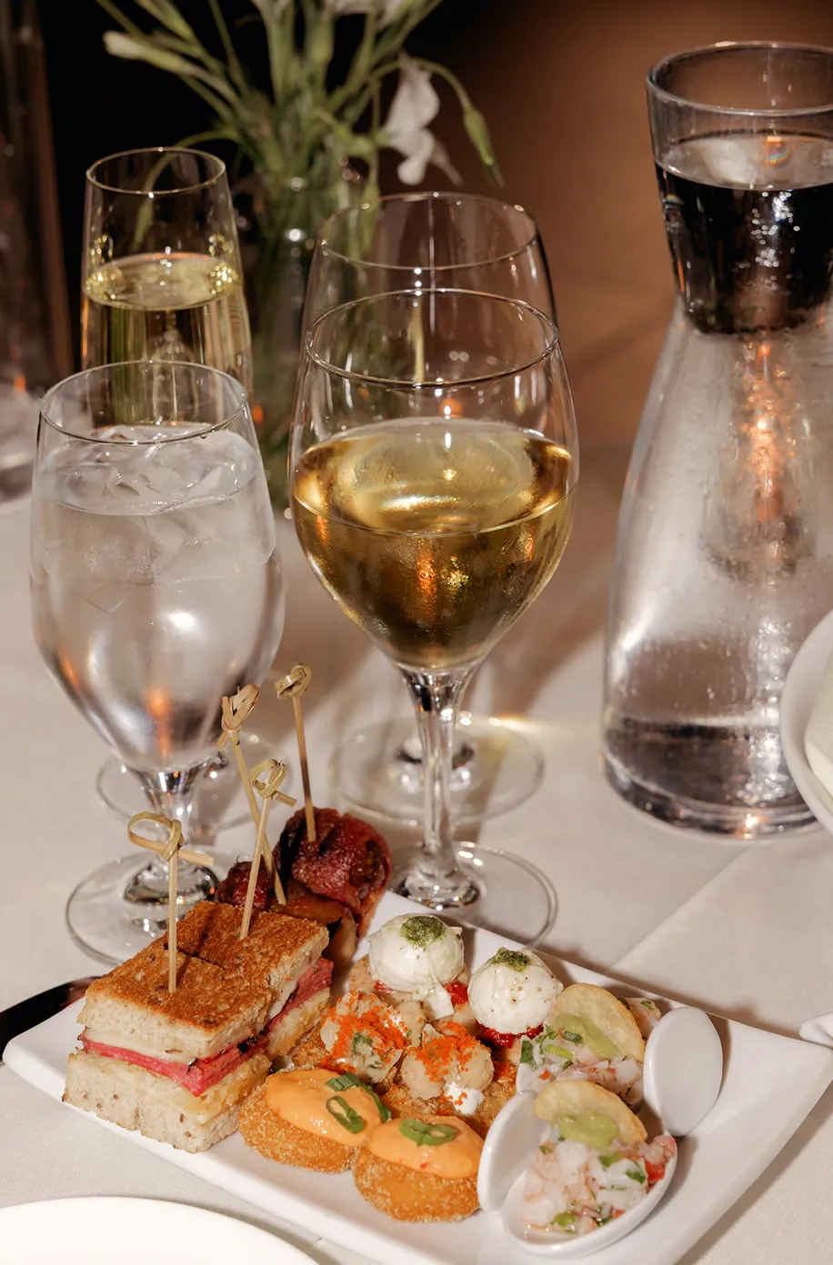 Assorted hors d'oeuvres and finger sandwiches on a tray with glasses of champagne and white wine