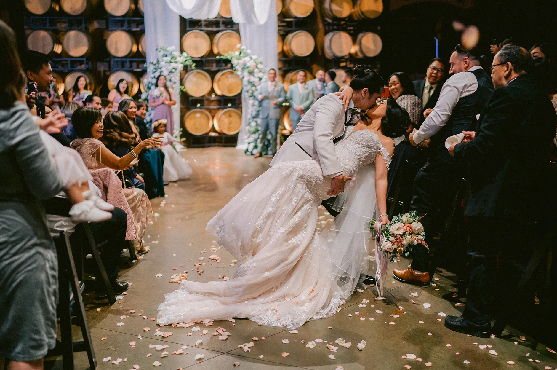 Groom dipping the bride for a kiss as they walk back up the aisle past cheering guests in the barrel room