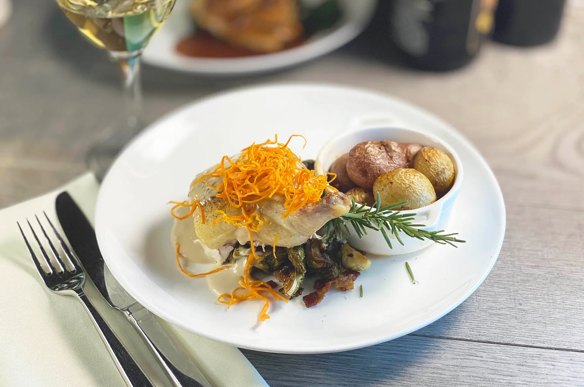 Roasted chicken with shredded carrot garnish, baby potatoes, and a rosemary sprig on a white plate