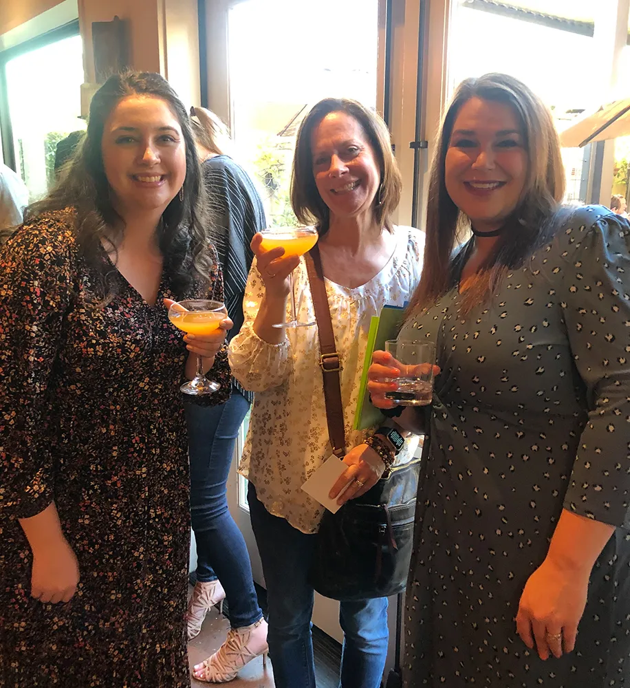 Three team members raising colorful cocktails together at a bar