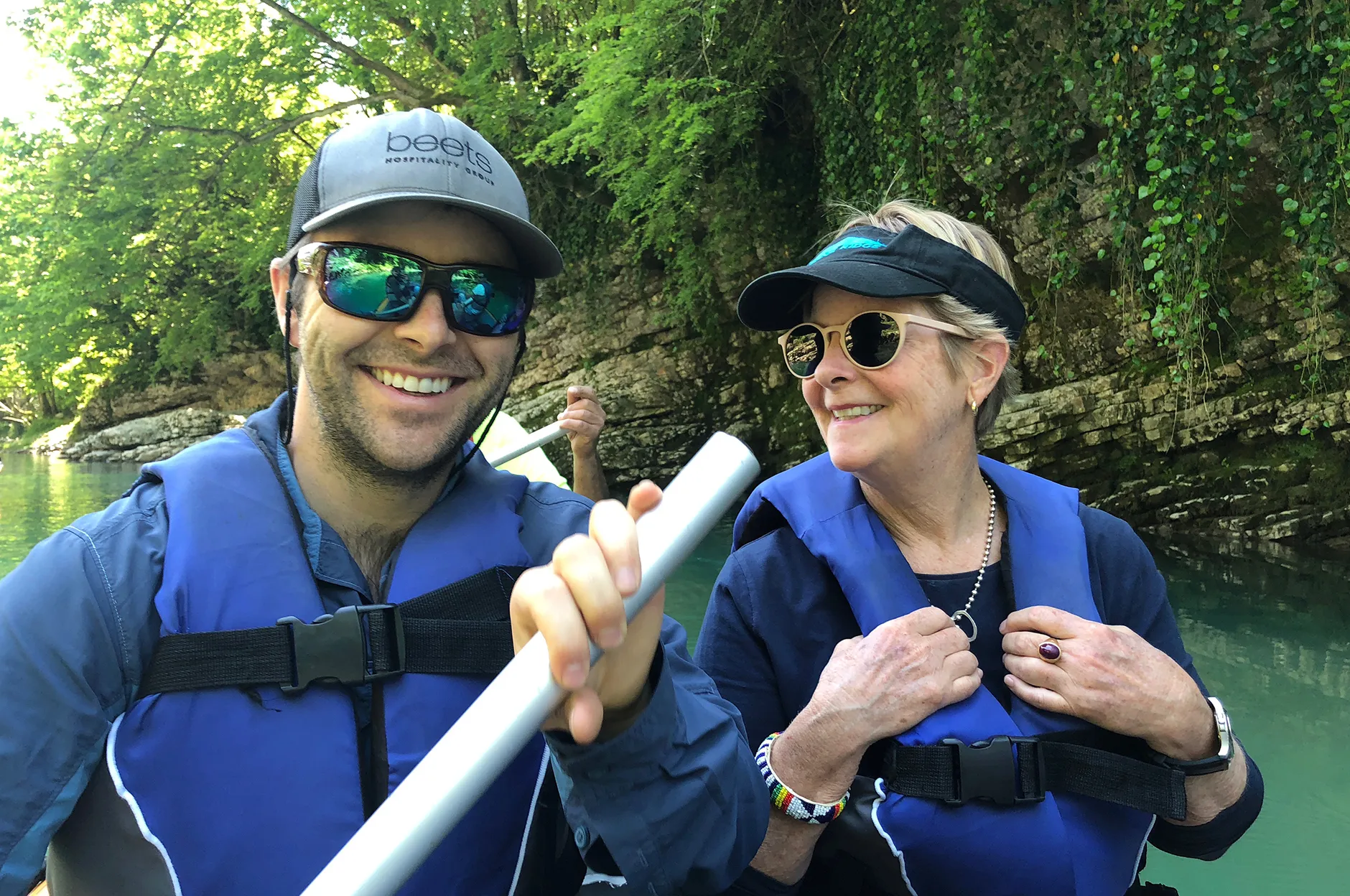 Two team members in life jackets and sunglasses paddling a kayak on a green river