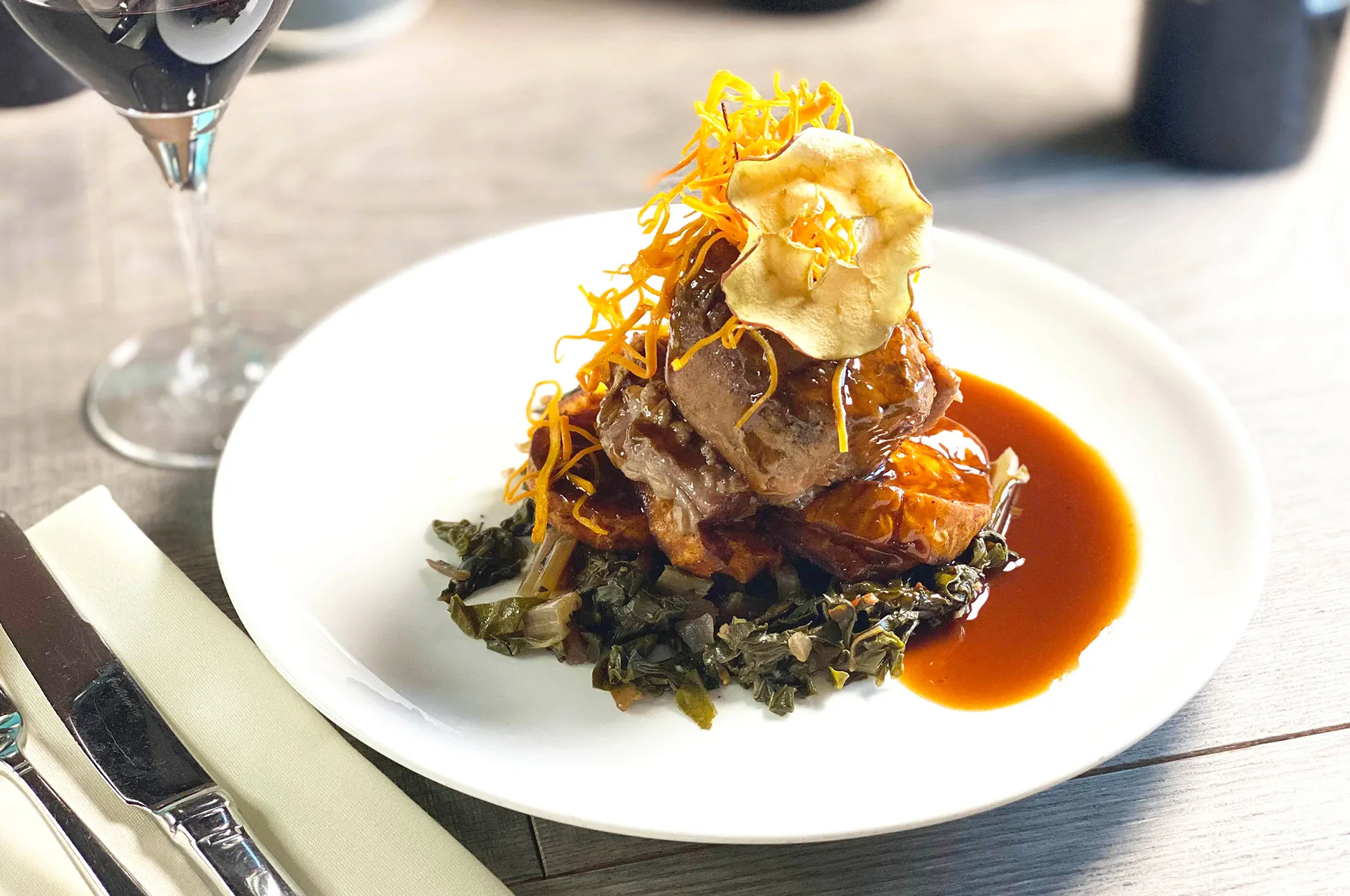 Braised pork over sautéed greens topped with crispy garnish and a rich brown sauce