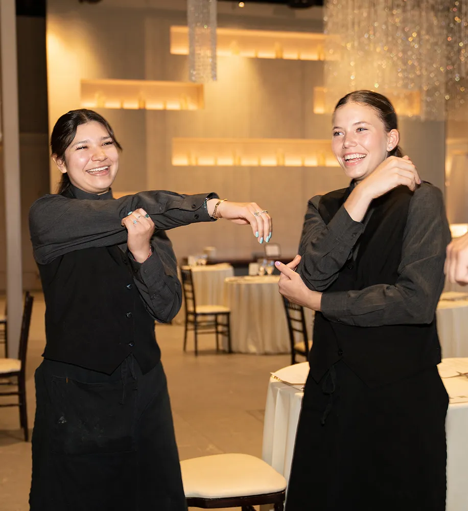 Two servers in black uniforms striking a fun pose together in the banquet hall between events