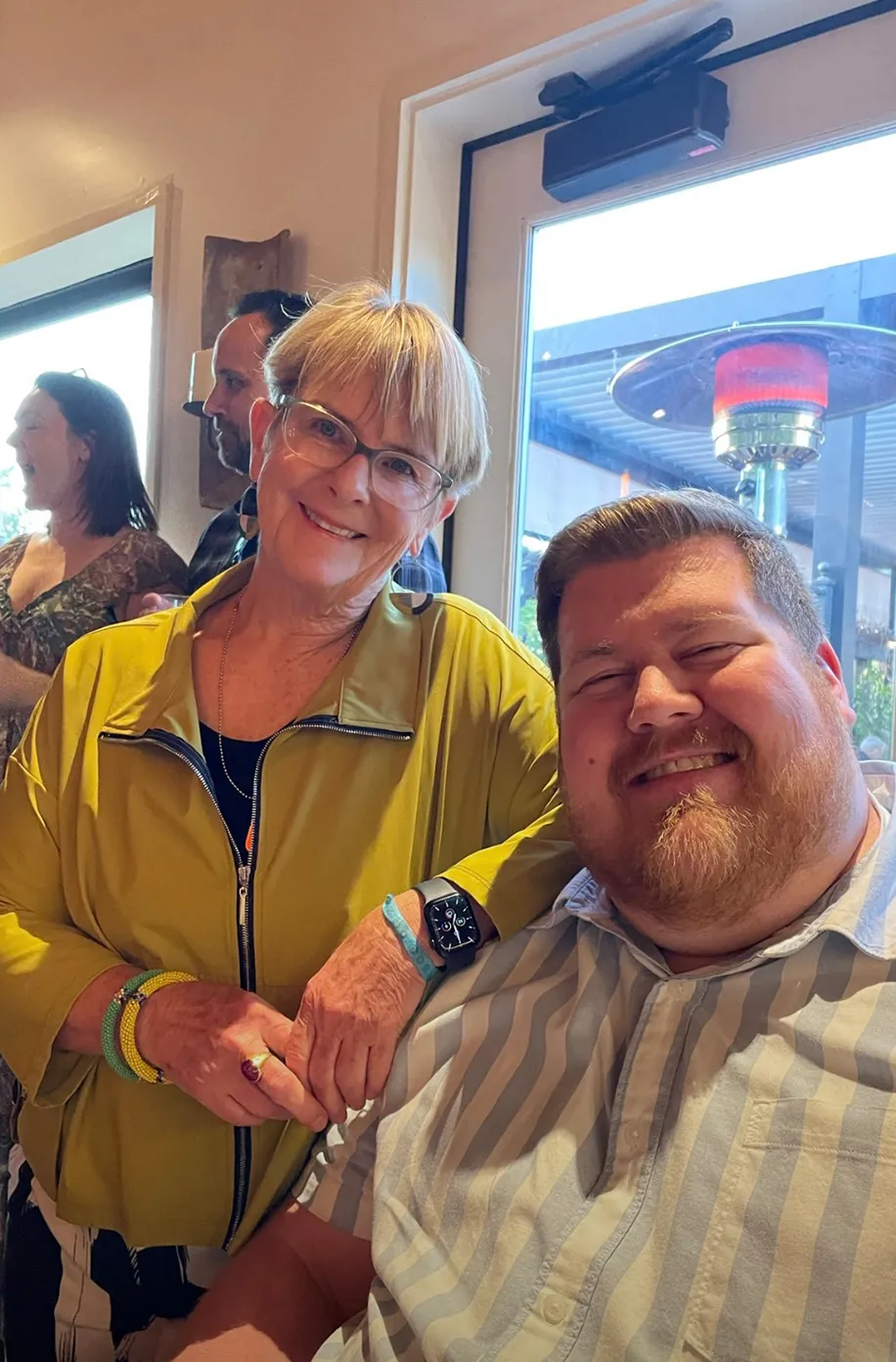 Two team members smiling together at a restaurant table on a sunny afternoon