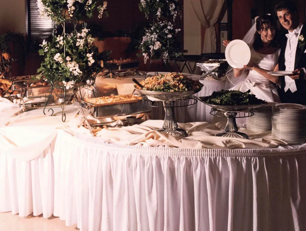 Beets catering buffet at The Shrine with chafing dishes, floral arrangements, and two team members behind the skirted table