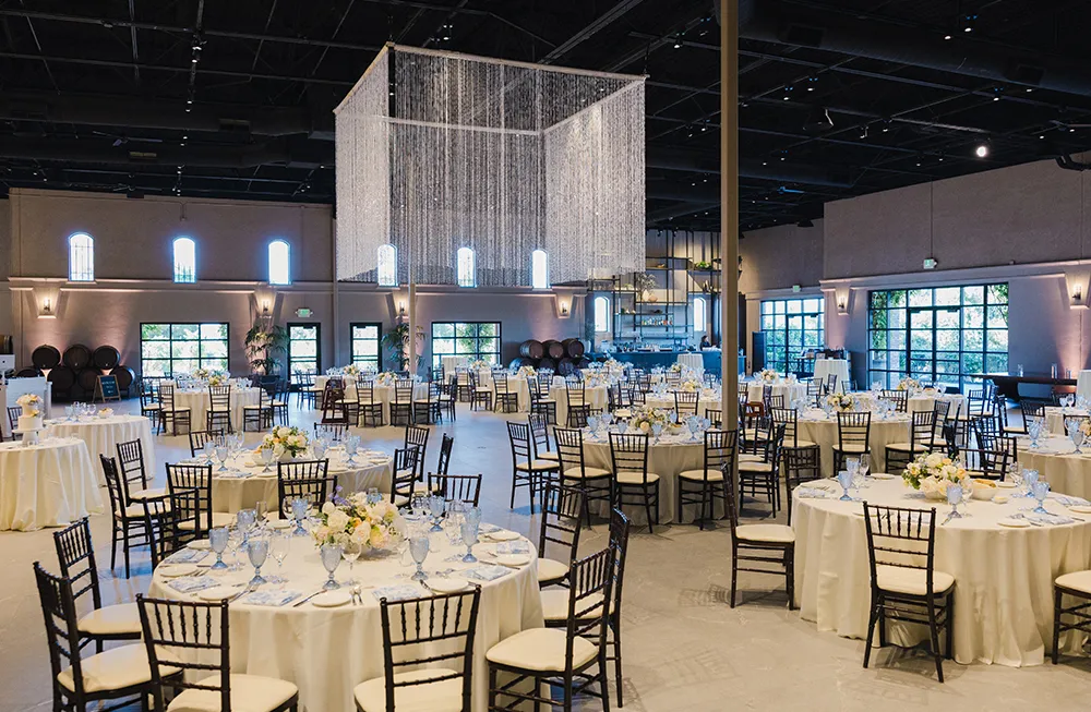 The Palm ballroom after renovation with round tables, black chiavari chairs, and a crystal curtain chandelier