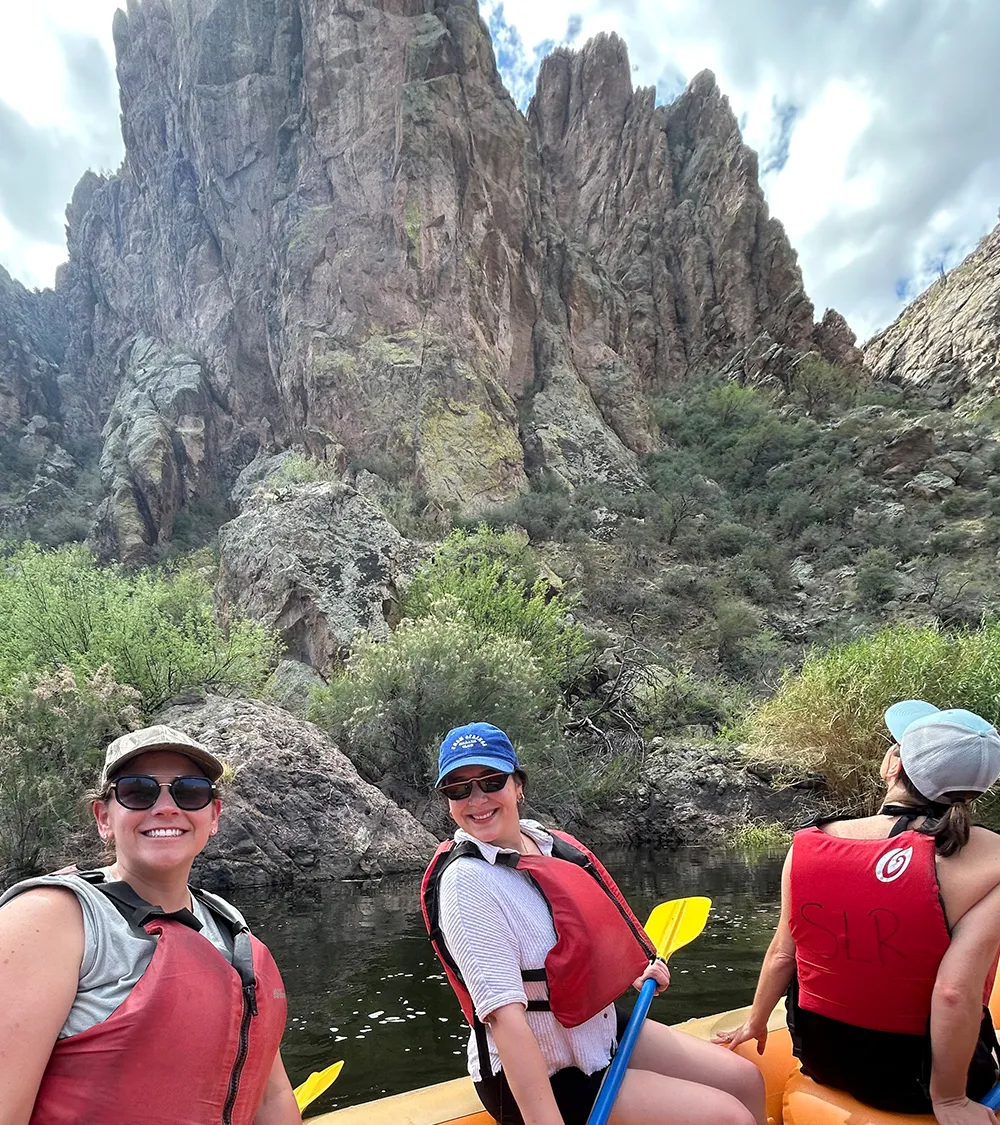 Team members kayaking together with desert cliffs in the background