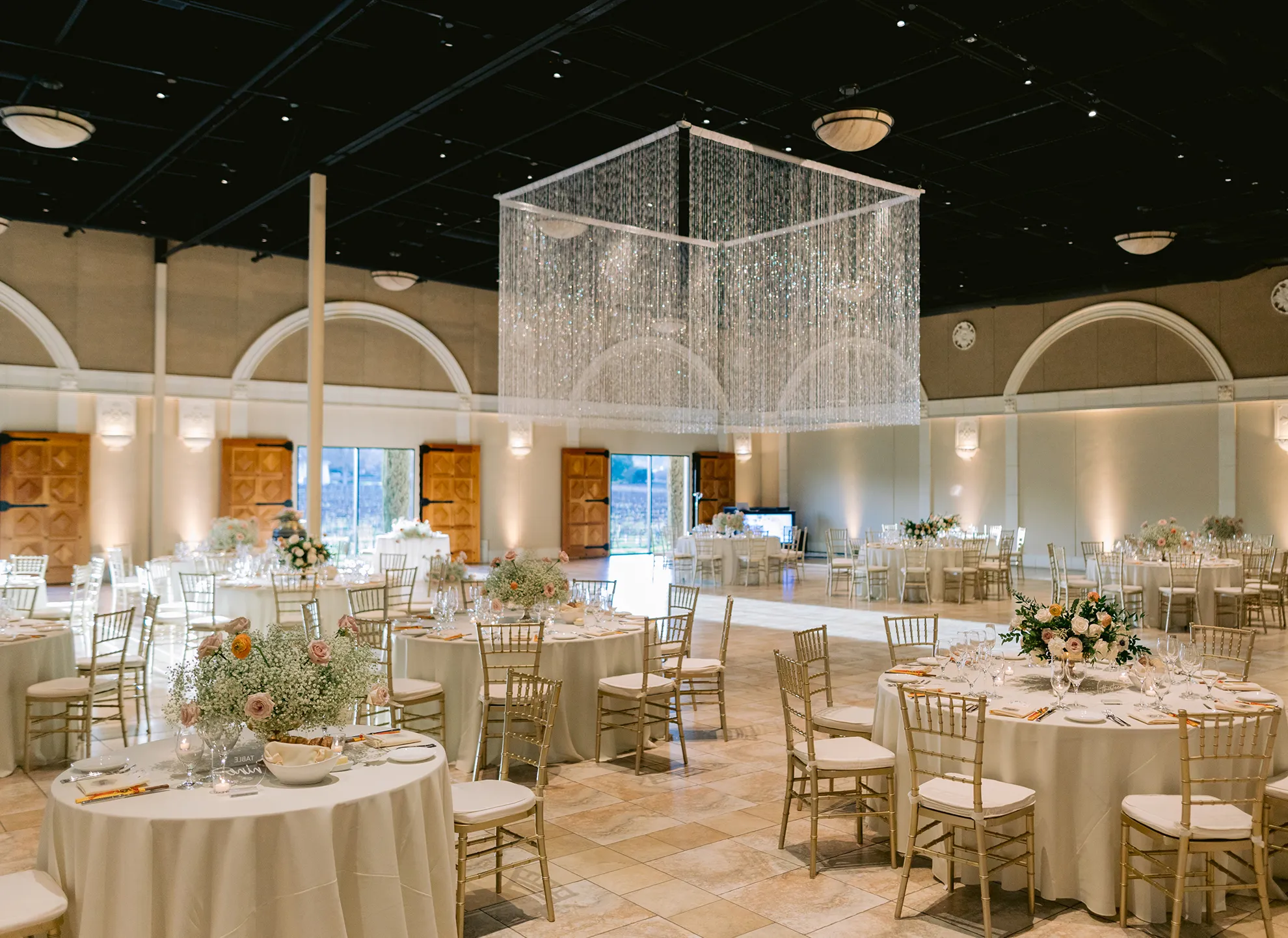 Grand Salon reception with round tables, gold chiavari chairs, floral centerpieces, and a crystal curtain chandelier