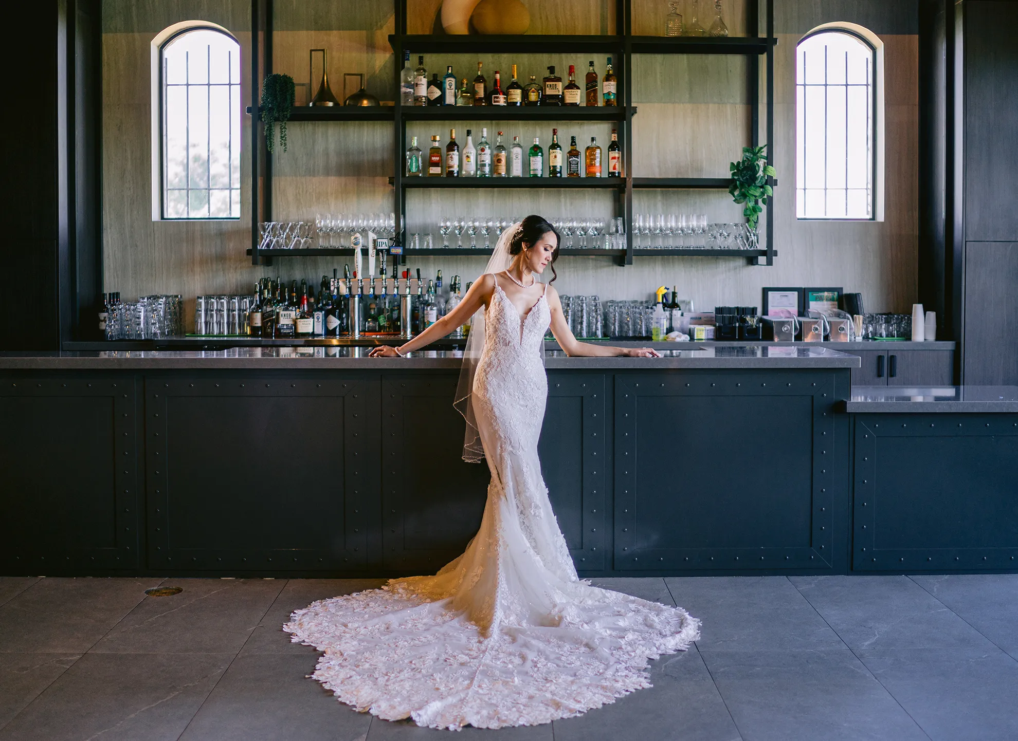 Bride posing in front of The Palm bar with dark cabinetry, backlit shelving, and arched windows