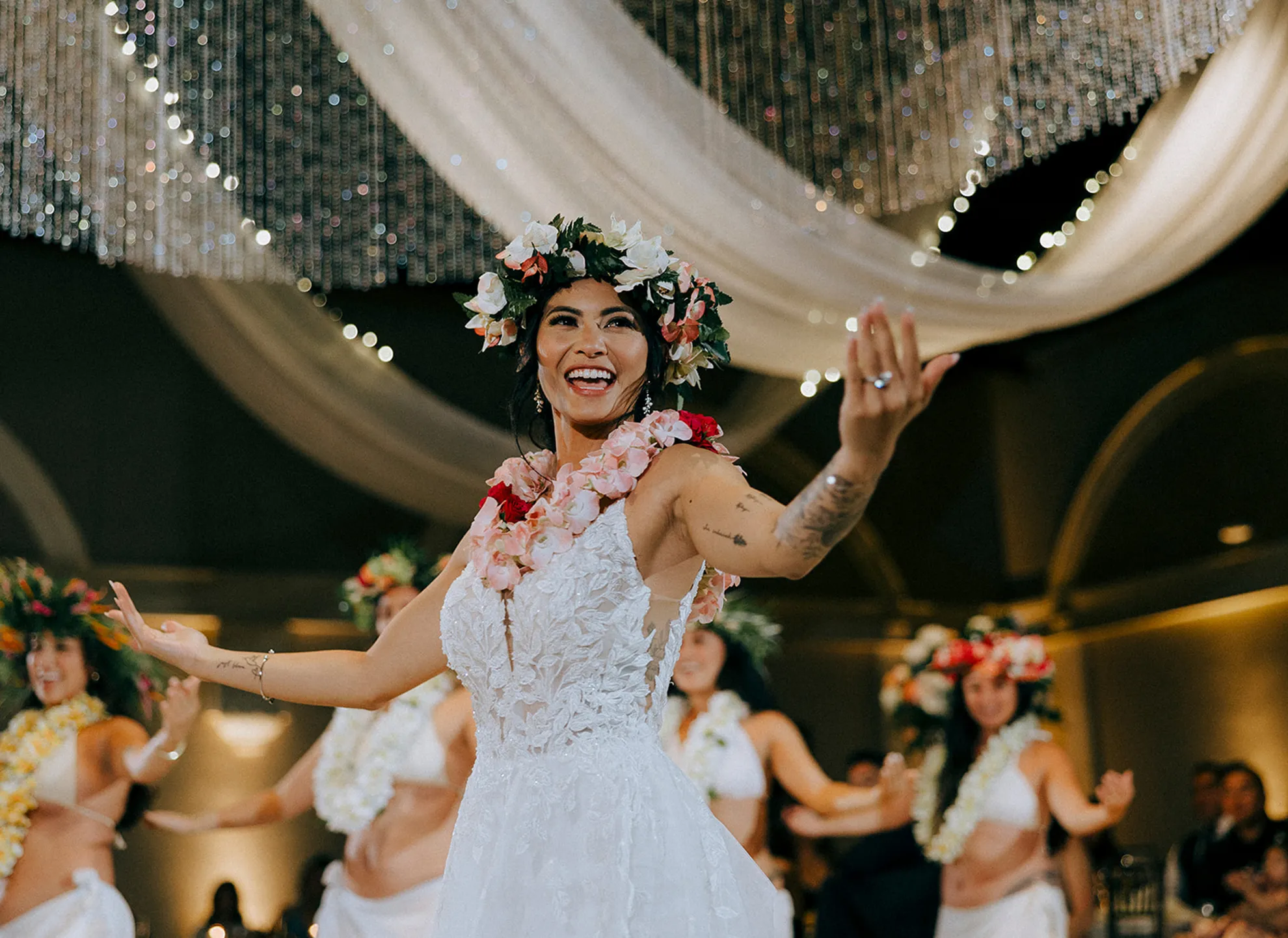 Bride wearing a flower crown celebrating with hula dancers at her reception